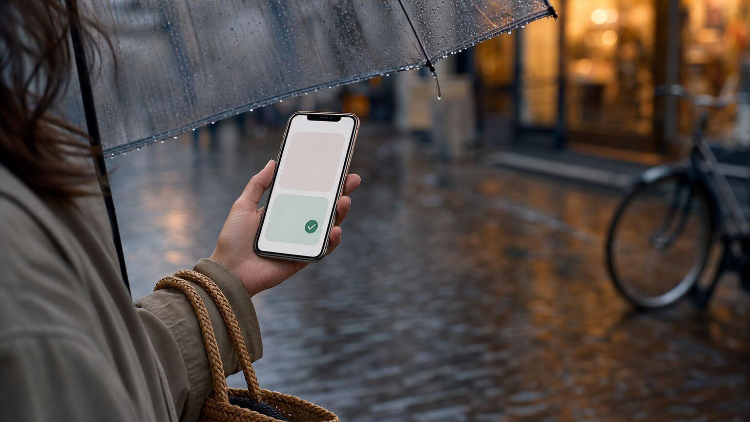 Hand met een smartphone onder een doorzichtige paraplu in een natte Nederlandse winkelstraat bij schemer